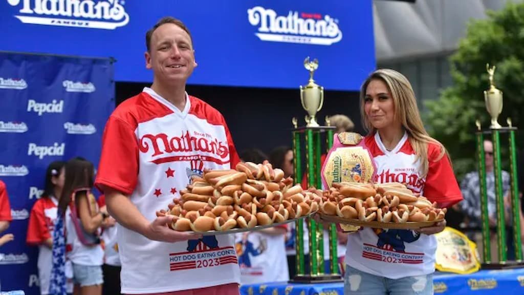 Joey Chestnut (left) and Miki Sudo (right) hold platters of hot dogs at the 2023 Nathan's Hot Dog Eating Contest - 2025 Nathan's Hot Dog Eating Contest Odds cover